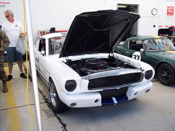 White race car, hood up, showing engine. Another green race car with number 27 is parked next to it