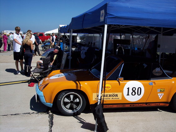 Orange race car with number 180 on door, under a blue tent at a race track