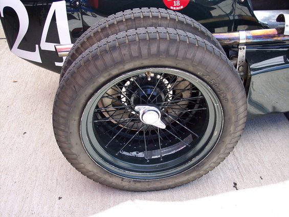 Close-up of a wire-spoke wheel and tire on a dark green racing car with the number 24 visible on the body