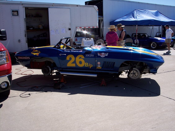 blue race car with yellow stripe, number 26, on jacks, with another blue car in background