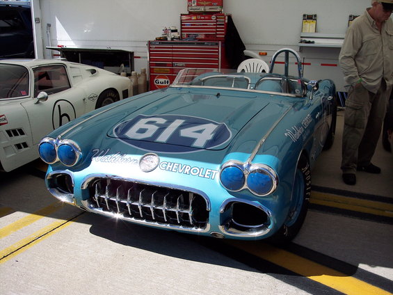Blue 1957 Chevrolet Corvette race car with number 614 on hood, parked next to a white car