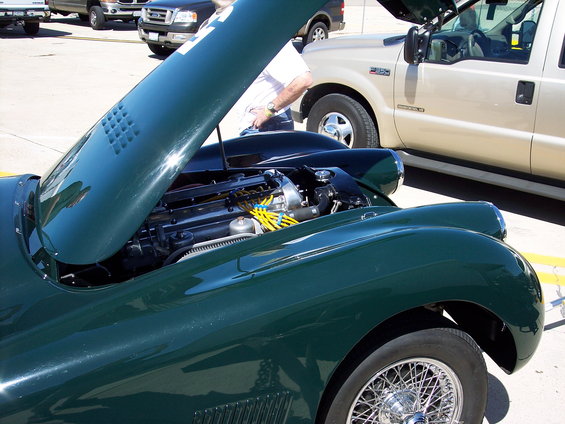 Green classic car with hood open showing engine. Other trucks are parked behind it