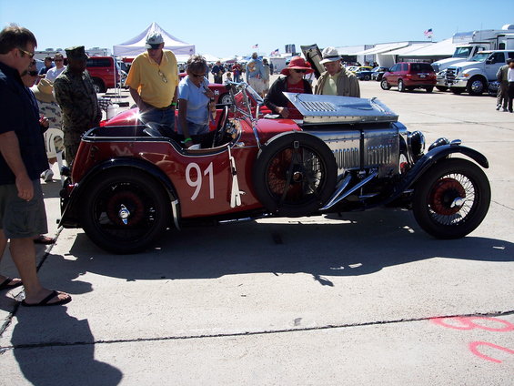 Red vintage race car with number 91 on the side, exposed engine, and spare tire