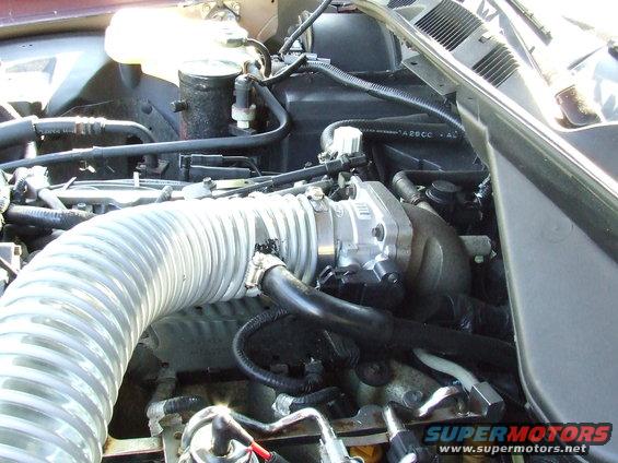 Engine bay showing a large, ribbed intake tube connected to the throttle body. Some hoses and wiring are visible