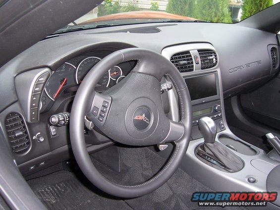 Corvette interior with steering wheel, dashboard, and center console visible. 'CORVETTE' text is embossed on the dash