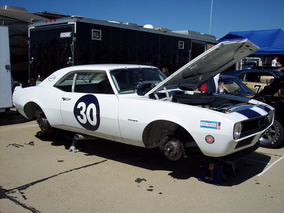 White 1968 Camaro race car with blue stripes, number 30 on door, hood open, on jack stands. Another car visible behind