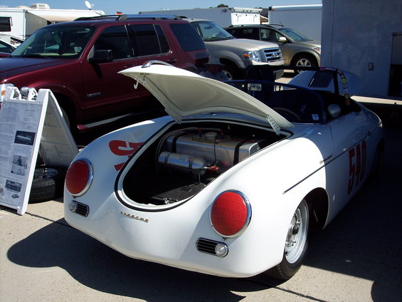 White Porsche 356 with hood open, showing fuel tanks. Red number 510 on side. Other vehicles and RVs in background
