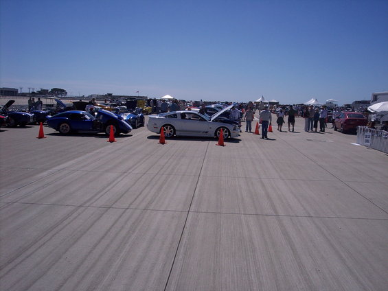 Cars parked on tarmac at an outdoor event, some with hoods open