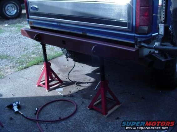 Red aftermarket bumper on a blue Ford truck, supported by red jack stands
