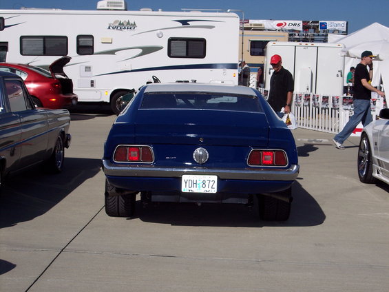 Rear view of a blue 1970s Ford Mustang with license plate YDH 872. Other vehicles and RVs are visible