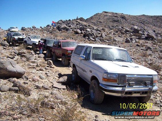 White 1992 Ford Bronco on rocky terrain, front 3/4 view, with other off-road vehicles behind
