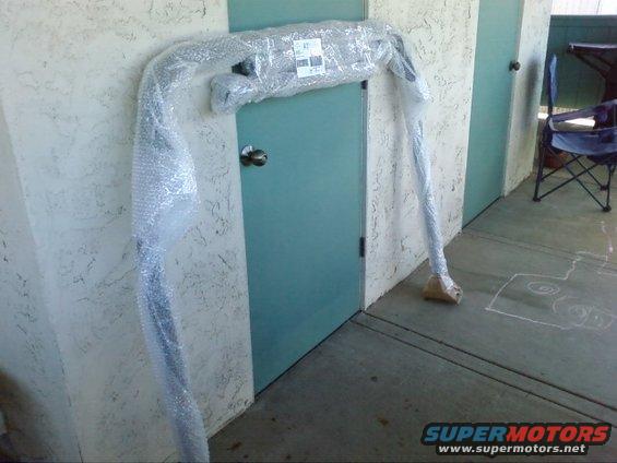 Wrapped car part leaning against a wall next to a teal door
