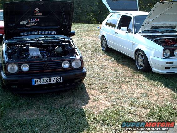 Black Volkswagen Golf with engine exposed, parked next to a white Golf with hood open. License plate MR XA 481