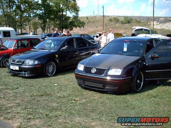 Black sedan with carbon fiber hood parked next to a red Mini and another black sedan