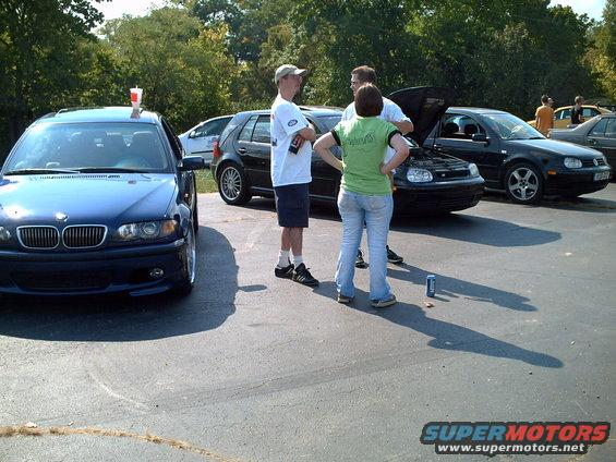 Blue BMW sedan front view with people gathered around other cars