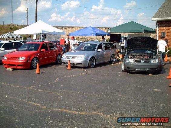 Red sedan, silver wagon, and gray sedan, all Volkswagen Jettas, parked outside under tents