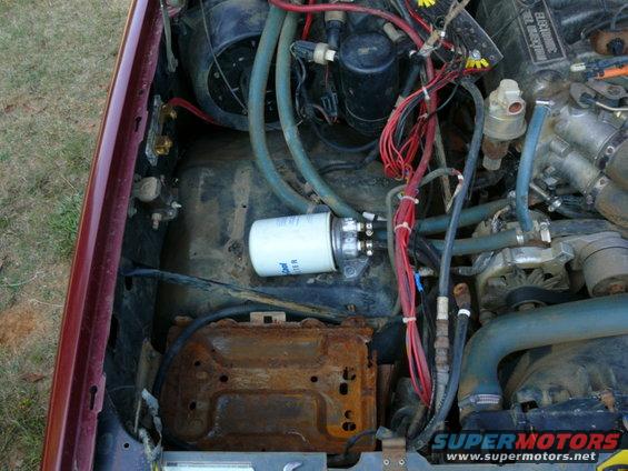 Engine bay showing a white fuel filter, rusty battery tray, and wiring