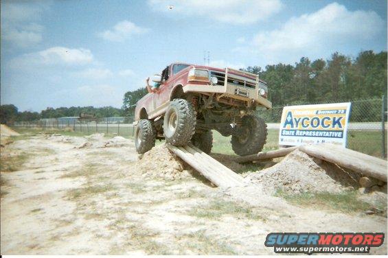 Red lifted Ford F-Series truck on wooden ramp, front grille visible