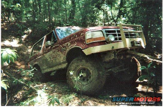 Red SUV stuck on a muddy hill in the woods, front bumper modified with a brush guard