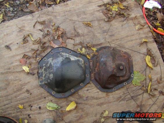 Two differential covers, one black and one rusty, on a wooden surface with fallen leaves