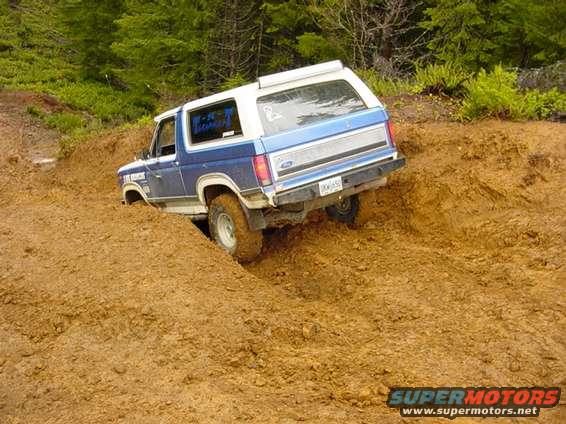 Blue and white Ford Bronco navigating a muddy incline
