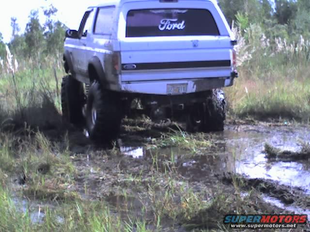 Rear view of a lifted 1995 Ford Bronco driving through mud and tall grass