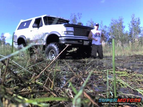 1995 Ford Bronco lifted and stuck in mud with a person standing next to it