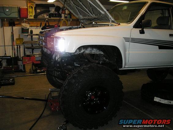 White pickup truck with hood open, lifted suspension, and large off-road tires
