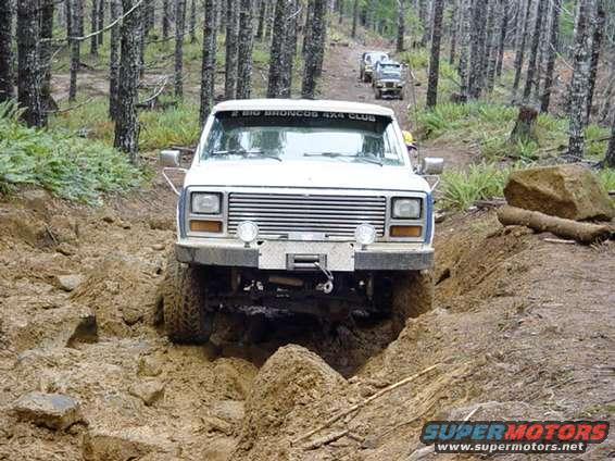 White Ford Bronco navigating a muddy trail with other vehicles behind it