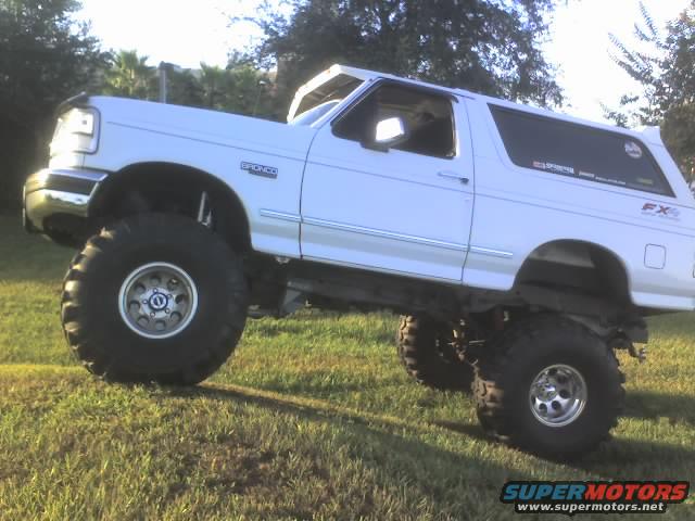 White Ford Bronco with lifted suspension and oversized tires parked on a grassy hill