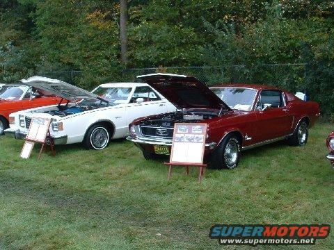 Red 1967 Ford Mustang coupe with hood open, parked on grass