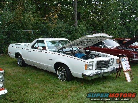 White Ford Ranchero with hood open, parked on grass next to a red car. Signboard in front of the white car