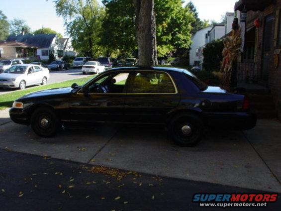 2003 Ford Crown Victoria parked on a paved driveway, side view. Other cars and houses are visible in the background