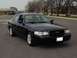 2003 Ford Crown Victoria - This black Ford Crown Victoria is parked in a lot with trees and buildings in the background.