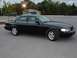 2003 Ford Crown Victoria - A black 2003 Ford Crown Victoria is parked in a lot with trees and a building in the background.