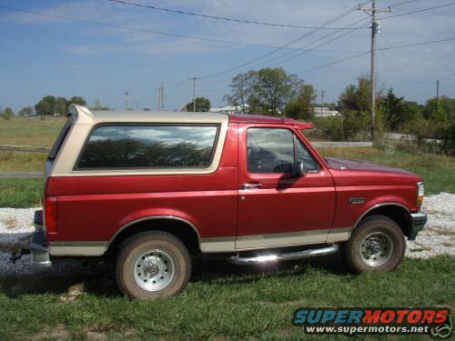 Red 1994 Ford Bronco with tan removable top, parked on grass and gravel