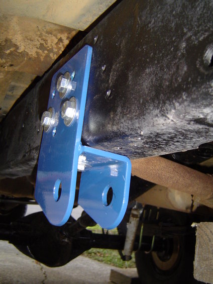 Blue metal bracket bolted to vehicle frame with visible suspension and axle components