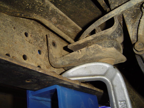 Close-up of rusty vehicle frame with a C-clamp and blue support