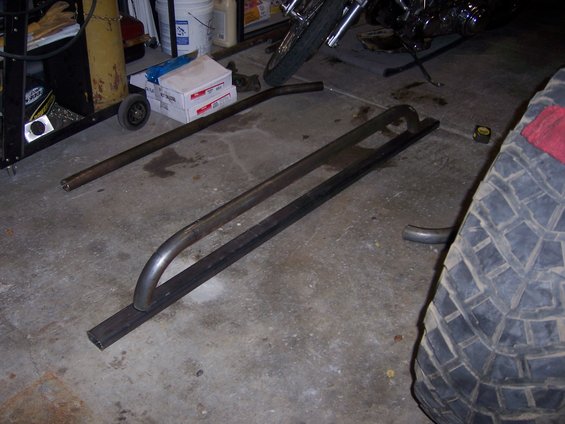 Metal tubes bent into slider shapes on a concrete floor, next to a large tire