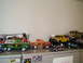 1979 Ford Bronco - A collection of toy vehicles, including a green and brown 1979 Ford Bronco with wood paneling, are displayed on a shelf.