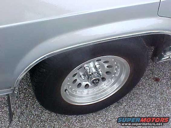Silver car fender and wheel with aftermarket rims. Text reads SUPERMOTORS.NET