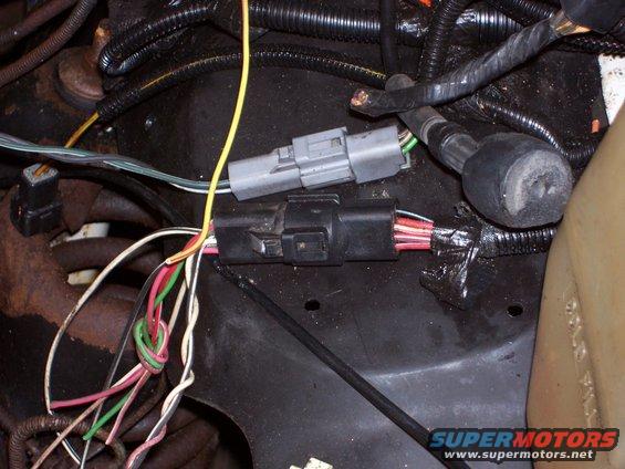 Engine bay wiring harness with two gray and black connectors, and bundled wires. Some tape is visible