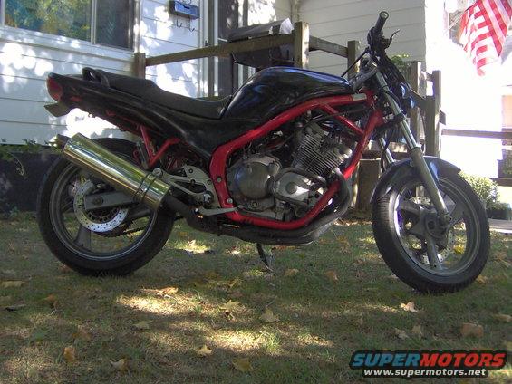 Motorcycle with red frame and black tank parked on grass. American flag visible