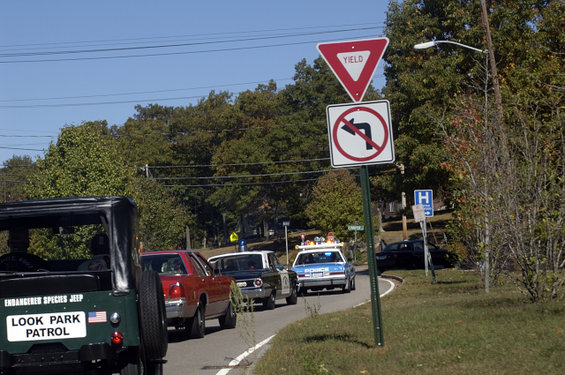 Green Jeep with 'Look Park Patrol' on the back, in traffic behind a red car and two police cars