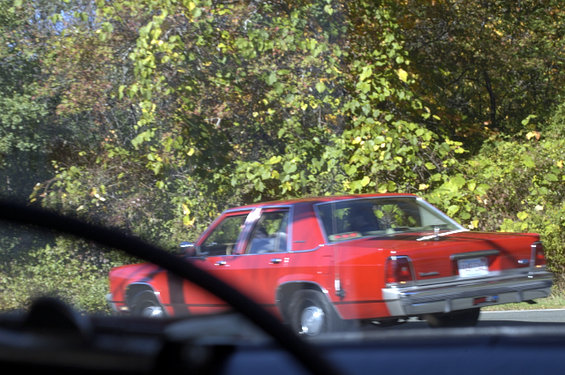 Red sedan driving on a road with trees in the background