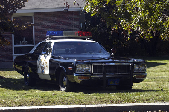 Black and white police car with light bar, parked on grass. California Highway Patrol markings visible
