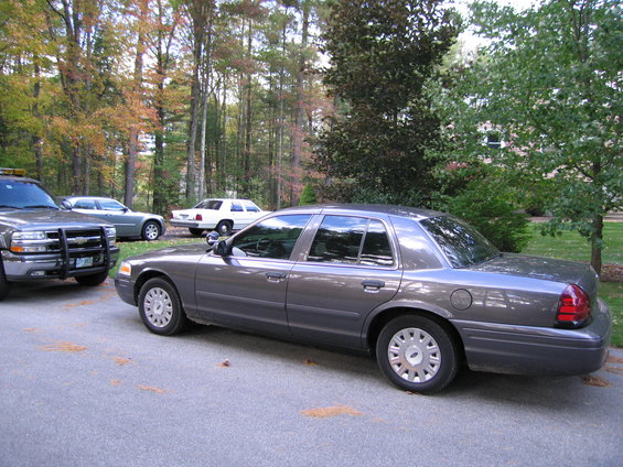 Gray Ford Crown Victoria parked on asphalt, another car and a truck visible