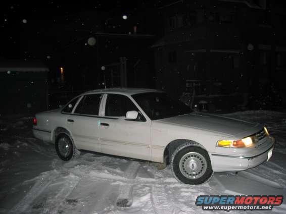White sedan parked in snow, 3/4 front view. Visible grille and headlights