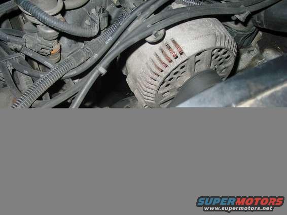 Close-up of an alternator with engine wiring and hoses