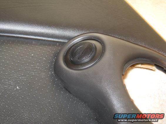 Black interior door panel with a small speaker grille and a visible SuperMotors.net watermark
